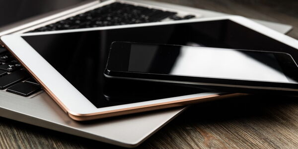 Laptop, Tablet und Smartphone liegen übereinander auf einem Holztisch