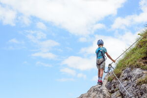 Ein Kind klettert an einem Seil gesichert auf einen Berg.