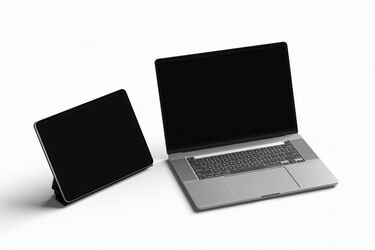 Silberner Laptop und schwarzes Tablet nebeneinander auf weißem Hintergrund.
